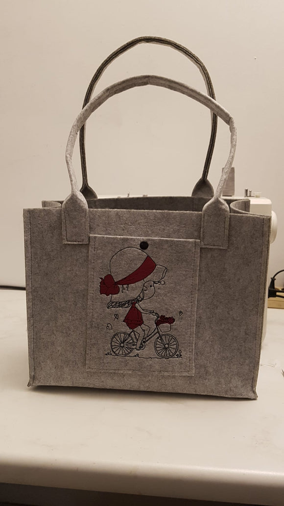 Filztasche aus hellgrauem Filz mit Fach vorne bestickt mit Mädchen auf Fahhrrad und mit Kam Snap Kunststoff-Druckknopf