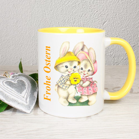 Tasse mit gelbem Henken und innen gelb, mit Frohe Ostern und Hasenpaar Motiv beidseitig bedruckt.